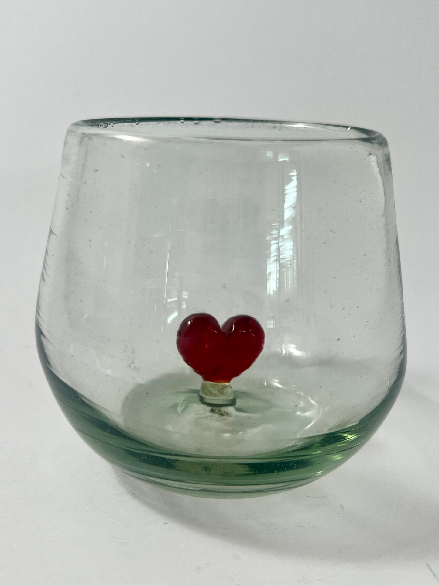 A clear glass wine glass with a figure of a red heart in the center, set against a white background.