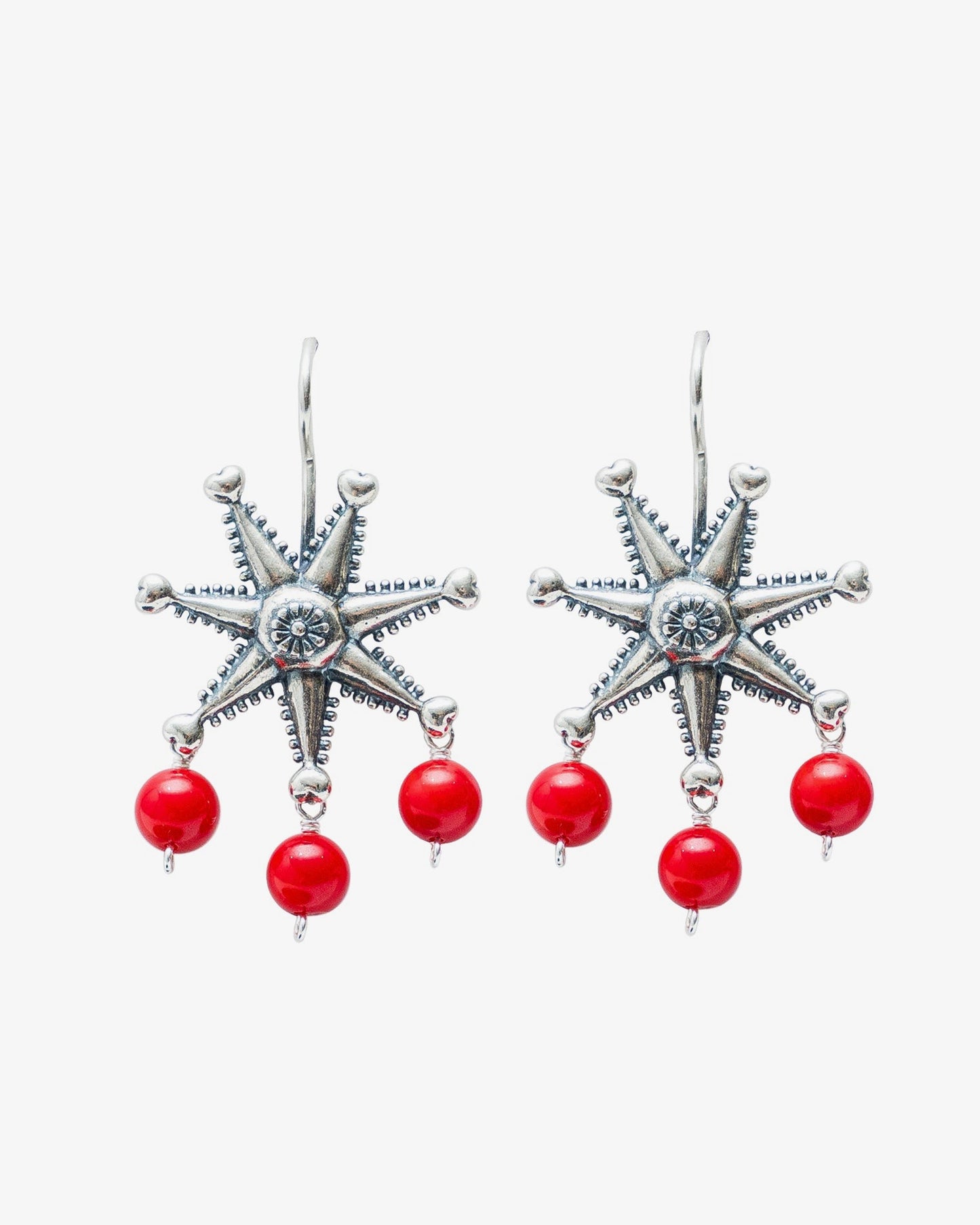 A pair of silver-toned dangle earrings featuring a six-pointed starburst design with a central clear stone and three dangling red beads below each star, shown on a light gray background.