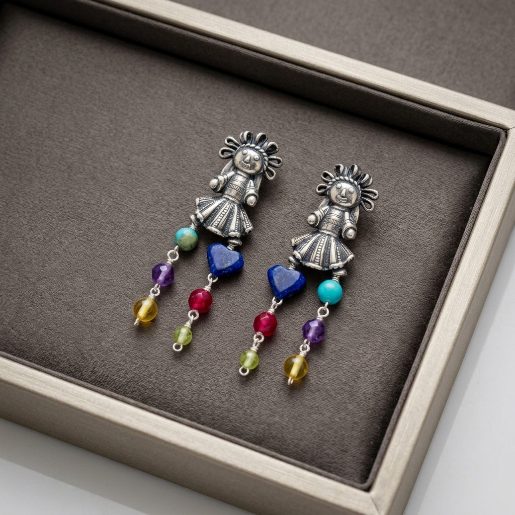 A pair of silver-toned dangle earrings displayed in a gray jewelry box. Each earring features a decorative silver figure charm with sun-like rays, a blue heart-shaped bead, and dangling multicolored beads in turquoise, purple, red, green, and yellow.