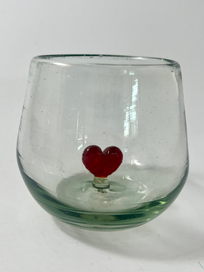 A clear glass wine glass with a figure of a red heart in the center, set against a white background.