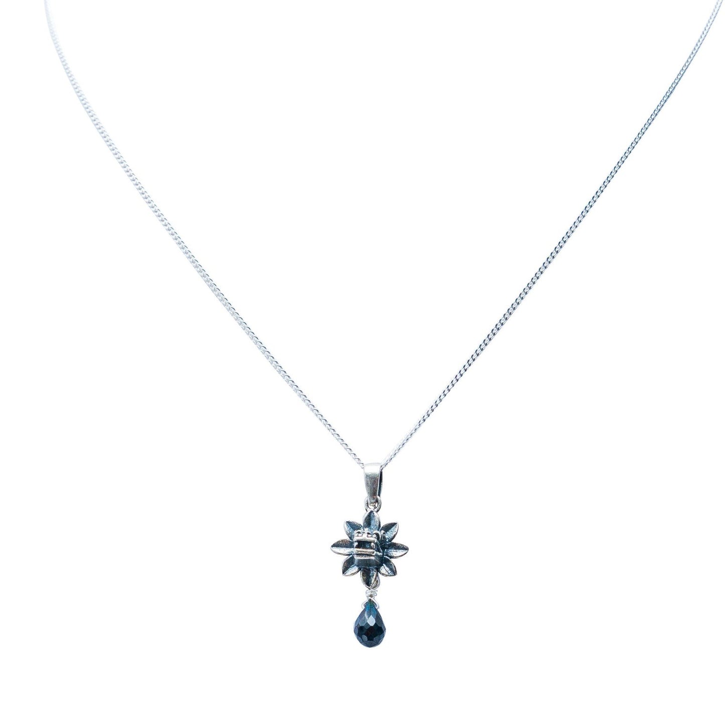 A silver-toned chain necklace featuring a starburst pendant with a dangling teardrop-shaped dark blue gemstone, set against a plain white background.