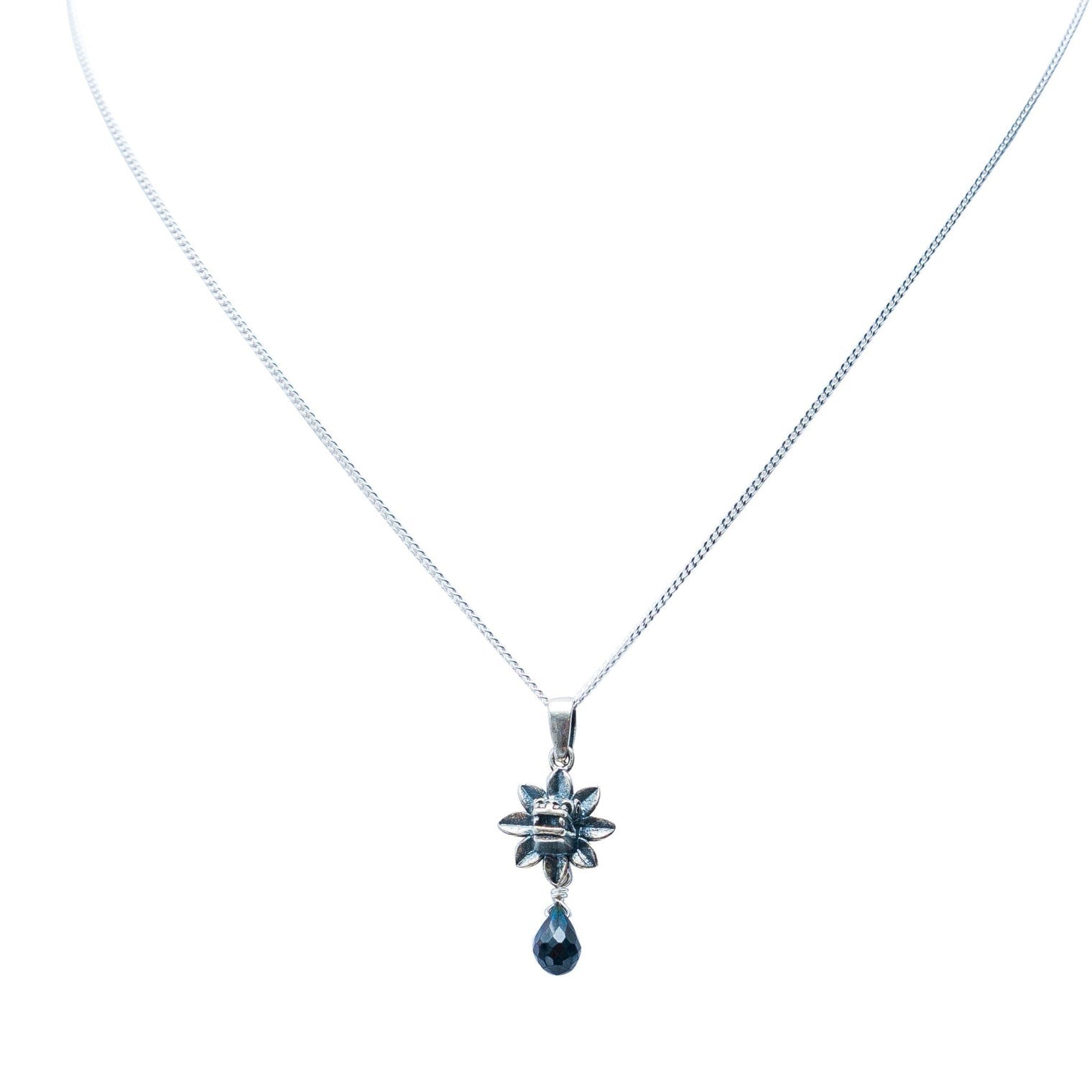 A silver-toned chain necklace featuring a starburst pendant with a dangling teardrop-shaped dark blue gemstone, set against a plain white background.