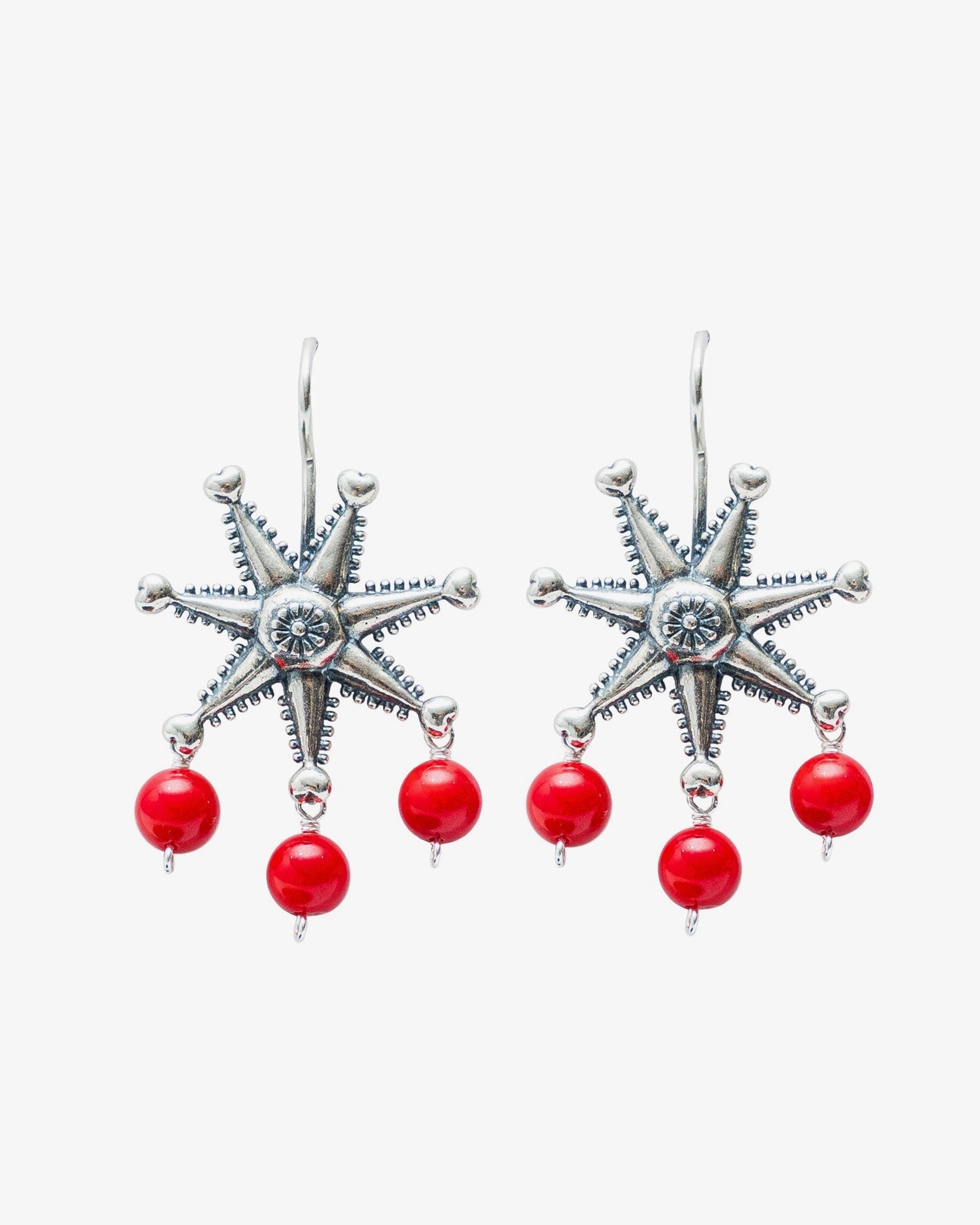 A pair of silver-toned dangle earrings featuring a six-pointed starburst design with a central clear stone and three dangling red beads below each star, shown on a light gray background.