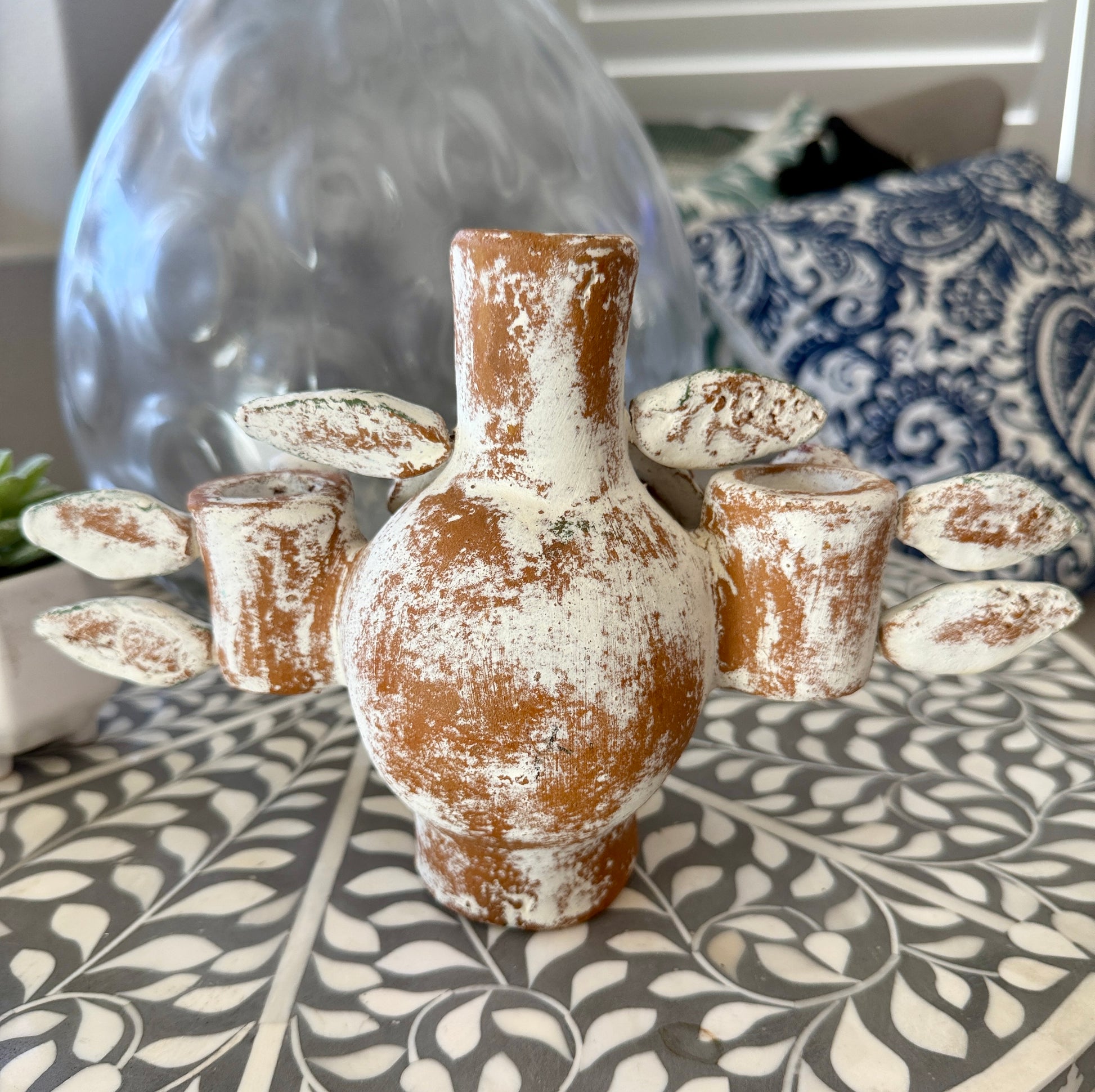 A rustic decorative cactus sculpture with a distressed brown and white finish, displayed on a patterned tablecloth in a home setting.