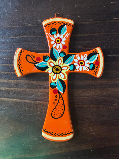 An orange wooden cross wall hanging decorated with colorful hand-painted floral and paisley patterns, shown on a dark wood background.