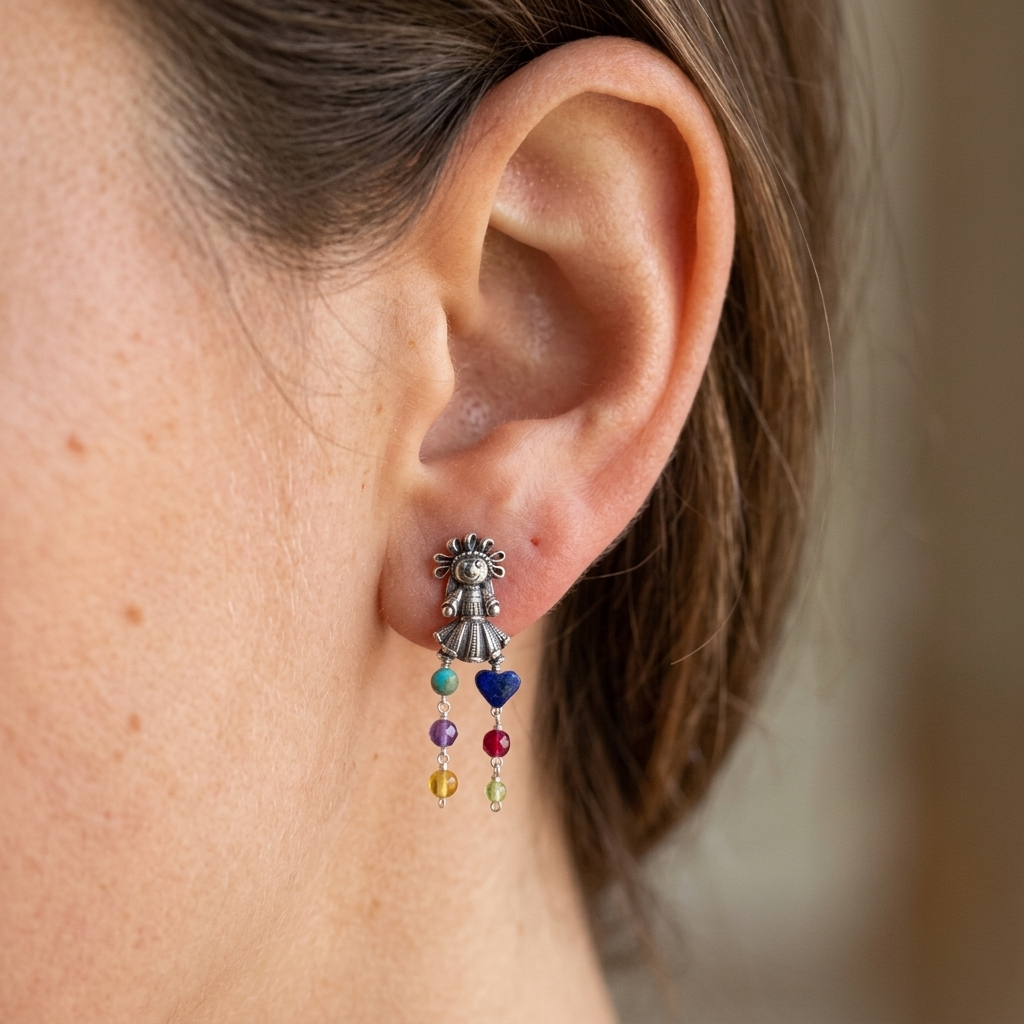 A close-up of a person's ear wearing a dangling earring. The earring has a silver-toned fairy charm at the top with small colorful beads dangling below, including blue, purple, red, yellow, and green.