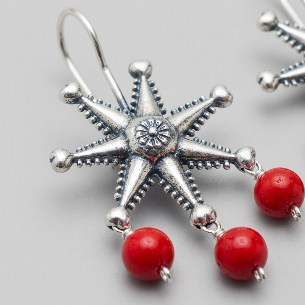 Silver-toned starburst dangle earrings with red bead drops, shown in a close-up studio shot on a light gray background.