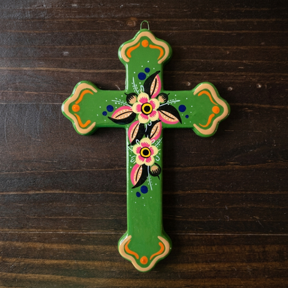 A hand-painted green ceramic cross with floral and geometric patterns, displayed on a dark wood background.