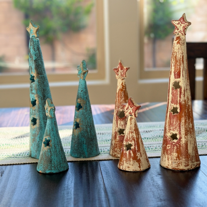 A set of six distressed decorative Christmas tree ornaments in teal and rust-red tones, arranged on a dark wooden table in front of a softly blurred window background.