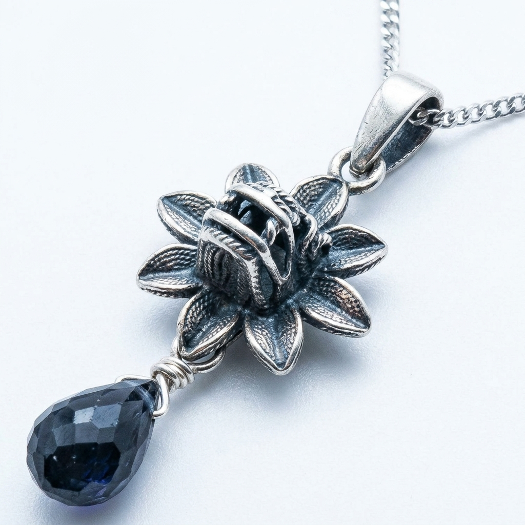 A silver-toned lotus flower pendant necklace with a faceted dark blue teardrop gemstone, shown on a white background.